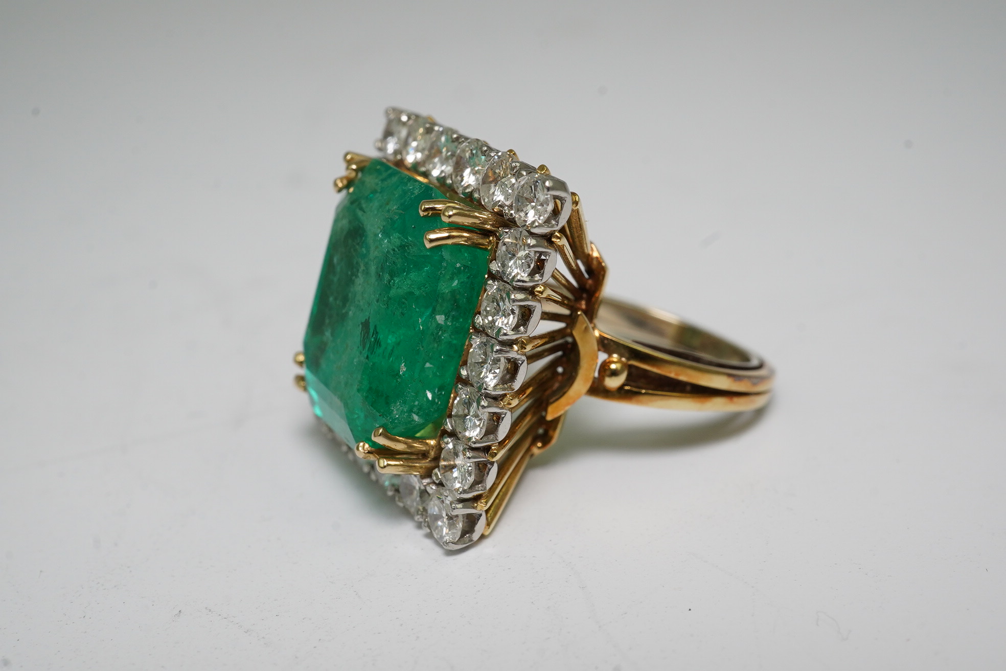 A Stern 18ct white and yellow gold, emerald and diamond dress ring, the central green emerald cut emerald approximately 8.0ct and surrounded by twenty two circular cut diamonds, approximately 2.7ct total